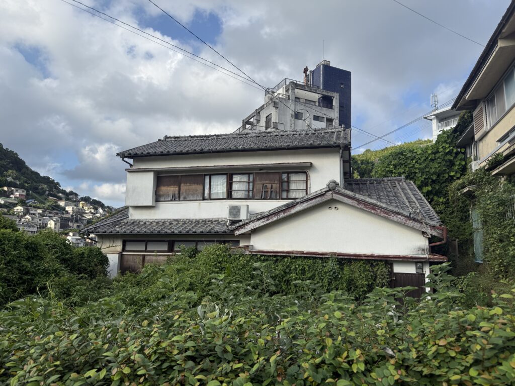 長崎で空き家を所有している方の中には、「手元に残すか、手放すか悩んでいる」「手放したいけど買い手がつかない」とお悩みの方もいらっしゃると思います。特に思い入れの強い空き家であれば、その扱いに迷われるでしょう。
そんなとき考えていただきたいのが、空き家を譲渡するという選択肢です。譲渡とは、売却のように利益を目的とせず、管理できない空き家を再活用してくれる人や団体へ引き継ぐ方法です。
この記事では、長崎で空き家を所有している方に向けて、空き家を譲渡する方法を詳しく解説します。空き家を放置するリスクから、注意点や税金の取り扱い、実際の再生事例まで紹介します。空き家の行き先に悩む方に、ぜひ読んでいただきたい内容です。
空き家を放置すると発生する3つのリスク
「使っていない家だけど、放っておいても問題ない」と考えていませんか?空き家を放置すると、所有者の責任として避けられないリスクが発生します。主なリスクは、以下の3点です。
<税金負担>
空き家を所有している限り、たとえ居住していなくても固定資産税や都市計画税の支払い義務が発生します。
通常、住宅が建っている土地は固定資産税が最大6分の1に軽減されますが、倒壊の危険があるなどの「特定空き家」に指定されると、この軽減措置が解除されてしまいます。2023年12月に改正された「空家等対策の推進に関する特別措置法」(改正空き家特措法)により、その前の段階である「管理不全空き家」に指定された場合でも解除の対象となりました。
管理されていない空き家は、税金の負担が重くなるのです。
<倒壊の恐れ>
老朽化した空き家では、屋根の崩落や外壁の剥離、雨漏りによる腐食などが進行し、倒壊するリスクが高まります。実際に、台風や地震で倒壊する事例をニュースで目にされたことがあるでしょう。
市町村は「空家等対策特別措置法」に基づき、危険と判断された建物に修繕・撤去の勧告や命令を出すことができます。従わない場合は行政代執行で解体され、費用が所有者に請求されるケースもあります。
草が生えすぎて、室内に入り込んでいます。
<賠償責任>
放置された空き家は、ゴミが溜まったり雑草が繁茂したりすると、害虫の発生や景観悪化を招く要因です。建物の一部が落下する、倒壊するなどして人や車を傷つける可能性も否定できません。空き家を放置すると、近隣にまで迷惑をかける恐れがあるのです。
民法717条(土地の工作物等の占有者及び所有者の責任)により、建物の所有者は第三者に与えた損害について無過失責任を負います。つまり、所有者に過失がなくても、建物の不備による被害について賠償責任が生じます。
このように、空き家を持ち続けて放置すると、経済的にも法的にもリスクがあるのです。
譲渡とは?売却との違い
放置するとリスクのある空き家を手放すと考えたとき、まず「売却」することが思い浮かぶでしょう。しかし、老朽化した建物や立地条件が悪い物件は、買い手がつきにくいのが現実です。そこで注目されるのが、「譲渡」という方法です。
売却は、所有者が金銭を受け取る行為です。買い手を探し、契約・決済を行い、市場価値に基づいた金額を受け取ります。
一方、譲渡は無償または極めて低い金額で空き家を引き渡す方法です。お金を得ることではなく、適切に管理・再生してくれる人に託すことが目的です。所有者は大きな金銭を受け取ることはできませんが、処分に困る空き家を手放すことで、さまざまなリスクから解放されます。
地域にもよりますが、安価な戸建を探している移住希望者や投資家のニーズが存在します。譲渡によって、リスクのある空き家を地域資源に変えることができるのです。特に長崎は、地形の制約があり宅地開発できるエリアが限られるため、空き家は移住希望者や投資家にとって魅力的な選択肢となり得ます。
譲渡は単なる引き渡しではなく、「誰に、どのような思い」で託すかを考える行為でもあります。思い出の詰まった家を解体するのではなく、次の世代に生かしてもらう視点を持つことで、譲渡は「手放す」から「地域へ託す」ことへと意味を変えます。
長崎で空き家を譲渡する3つの方法
「空き家を譲渡したいけれど、どうすれば良いのだろう?」と疑問に思われる方も多いと思います。そこで、長崎で選べる3つのルートを紹介します。
<「空き家バンク」を活用する>
もっとも安心なのが、自治体が運営する「空き家バンク」制度です。長崎でも、長崎市・諫早市・島原市から島しょ部まで、各地で導入されています。
空き家バンクは、空き家を売りたい・貸したい所有者と、住みたい・活用したい人をマッチングする仕組みです。空き家の所有者が自治体に登録を申告し、自治体による現地確認を受け、写真や所在地などの情報をウェブサイトに掲載します。売買だけでなく、無償譲渡の登録も可能で、登録料や仲介手数料もかかりません。
マッチングに時間がかかる場合もありますが、公的な仕組みのため、安心して利用できるのもメリットです。全国どこからでもウェブサイトを閲覧できるため、空き家を探す移住希望者や投資家の多くは、まず空き家バンクをチェックします。
空き家バンクは、長崎で空き家を譲渡する際にぜひとも活用したい手段です。
参考:長崎市移住・定住応援公式サイトながさき人になろう「空き家・空き地情報バンク(空き家バンク)」
<不動産会社に依頼する>
譲渡に対応する不動産会社はほぼ見られませんが、なかには無償譲渡に対応している会社も存在します。不動産会社を頼ることができれば、空き家再生に積極的な投資家やリノベーション会社とつながるチャンスがあります。
不動産会社に相談する際は、物件の状態や登記上の名義、相続関係を整理しておくとスムーズです。
当社は長崎市を拠点とし、空き家を住宅として再生しています。空き家を手放したい方は、ぜひお気軽にご相談ください。
<NPO・個人投資家に引き継ぐ>
地域で空き家再生に取り組むNPO法人やまちづくり団体に引き継ぐ選択肢もあります。このような団体の目的は、空き家をリノベーションして住まいやコミュニティ拠点に再生し、地域資源として活かすことです。
また、空き家のリノベーションに投資する個人投資家も存在します。
譲渡は、誰に託すかが重要です。譲渡を考えている空き家には、何かしら思い出や思い入れがある方が多いでしょう。地域とつながりを持つ団体や事業者に託すことで、家が再び息を吹き返します。
譲渡の注意点と税金の取り扱い
譲渡にはさまざまなメリットがありますが、いくつかの注意点も存在します。ここでは、大きく3つの注意点を解説します。
<登記を確認しておく>
空き家を譲渡する際は、登記上の所有者を明確にする必要があります。もし、相続した空き家で相続登記をしていない場合、譲渡ができません。
2024年4月1日から、相続登記が義務化されました。相続で不動産を取得したら、その所有権の取得を知った日から3年以内に相続登記の申請をしなければなりません。正当な理由なく義務に違反すると、10万円以下の過料の適用対象となります。
また、複数人で共有している空き家を譲渡するには、全員の同意が必要です。自分の持分だけ譲渡することは可能ですが複雑になるため、専門家へ相談することをおすすめします。
さらに、譲渡する際は所有権の移転登記が必要です。所有者権の移転登記をすることで、その不動産の正当な所有者を法的に明確にし、第三者に対して所有権を主張できるようになります。
固定資産税は登記上の所有者に課税されます。そのため、所有権移転登記を行わなければ、譲渡後も税金を支払い続けなければなりません。
<個人間の取り引きによるリスクがある>
空き家の譲渡においては、不動産会社を通さずに個人間での取り引きとなるケースが大半を占めます。空き家バンクを活用する場合も同様です。マッチングを手助けしてもらっても、最終的な契約手続きは当事者同士ですることになります。
所有権の移転登記や契約の手続きまで、すべて自分で行わなければなりません。仲介業者が入らない分、スピーディーに話が進められる面がある一方で、労力がかかりす。不動産取り引きには専門的な知識を要するため、専門家不在で進めるとトラブルが発生しやすいです。
<譲渡後のトラブルを未然に防ぐ>
空き家には、譲渡が済んだ後にトラブルとなるリスクが潜んでいます。見えない部分の腐食が見つかるといった重大な欠陥があった場合、契約不適合責任を問われる可能性もあります。譲渡後のトラブルを防ぐには、事前にしっかりと確認しておくことが大切です。近隣や境界の問題なども含めて、事前の調査と告知を怠らないようにしましょう。
譲渡後に、「家を壊されてしまった」「想定していた用途と違った」といったトラブルも起こりかねません。トラブルを防ぎ、譲渡人と譲受人の双方が気持ち良く取り引きするために、契約書を作成して譲渡条件を明記することが重要です。
上記の3点が、空き家を譲渡するときの主な注意点です。加えて、税金の取り扱いについても確認しておきましょう。
空き家を譲渡する場合、方法や条件によって税金が発生する可能性があります。
まずチェックしておきたいのは、譲渡所得税です。譲渡所得税は、不動産を売却して利益(譲渡所得)を得た際に課税されます。譲渡所得は「不動産の売却価格-(取得費+譲渡費用)」で算出され、無償譲渡や著しく低い価格での譲渡であれば、譲渡所得はゼロまたはマイナスとなります。そのため、空き家の譲渡において、譲渡所得税は発生しない場合がほとんどです。
なお、相続で取得した空き家を売却・譲渡する場合、「被相続人居住用財産の譲渡特例(3,000万円控除)」が適用できるケースもあります。
注意しなければならないのは、贈与税です。個人に対して無償で空き家を譲渡すると、譲受人に贈与税が課税される可能性があります。年間110万円までの譲渡であれば贈与税は発生しませんが、不動産の評価額がそれを超える場合には、譲受人が贈与税を納めなければなりません。
税金の取り扱いは複雑で、ケースによって異なるため、専門家への相談をおすすめします。
実際の譲渡事例
最後に、相続された空き家を投資家が再生した事例を紹介します。
Aさんは、古い木造住宅を相続で受け継ぎました。しかし、Aさん自身は実家を離れて遠方に住んでいたため、管理が不十分になっていました。屋根が痛み、内部も老朽化して、草木が伸びて景観も悪化している状態です。年に数回、除草などのために遠方から訪れる交通費も負担となっていました。
老朽化した空き家には買い手がつかず、解体するにも200万円ほどかかるため踏み出せずにいました。その間、維持コストが重くのしかかり続けます。
そんな中、売却ではなく譲渡するという方法を知り、譲受人を探したところ、投資家のBさんとつながりました。Bさんは、譲り受けた空き家をリノベーションし、住宅として再生。賃貸に出して、家賃収入を得ています。
一方、Aさんは管理負担や税金の支払いから解放されました。負担になってしまっていた大切な実家が、新たな住民に使ってもらえる家に生まれ変わったのです。防犯上のリスクが軽減され、景観も改善されたため、地域住民にとっても喜ばしいことでした。
所有者は負担から解放され、投資家や地域にとっては新しい価値が生まれたのです。
まとめ:空き家を手放すことは「地域に託す」選択肢
思い出が詰まった空き家、思い入れのある空き家を手放すことを躊躇する方もいらっしゃると思います。一方で、管理にかかる時間やお金を負担に感じている方も多いのではないでしょうか。
しかし、空き家は誰かに託すことで息を吹き返すことができます。空き家を譲渡することは、自らが管理や税金の負担から解放されるだけでなく、家が再生されて地域の資産となったり、伝統的な古民家が地域に受け継がれたりと、持続可能なまちづくりにつながる行動です。
空き家を手放すことは、「地域に託す」という選択肢です。空き家の扱いに悩んでいる方が、「譲渡」に関心を持っていただけたら幸いです。当社は長崎市を拠点に、空き家を次世代へ引き継ぐ事業を行っています。空き家を手放すことをお考えの方は、お気軽にご相談ください。